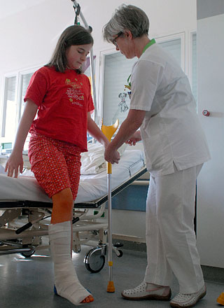 MÃ¤dchen mit Gipsbein steht an ihrem Bett. Schwester hilft beim Gehen