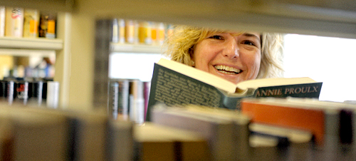 Frau mit Buch schaut durch ein BÃ¼cherregal